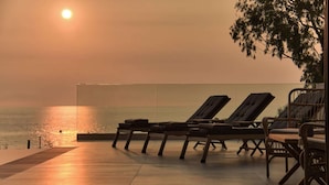 A sunset view from a balcony with lounge chairs and a pool.