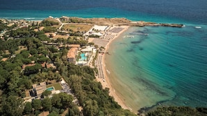 An aerial view of a coastal resort with a beach, pool, and surrounding greenery.