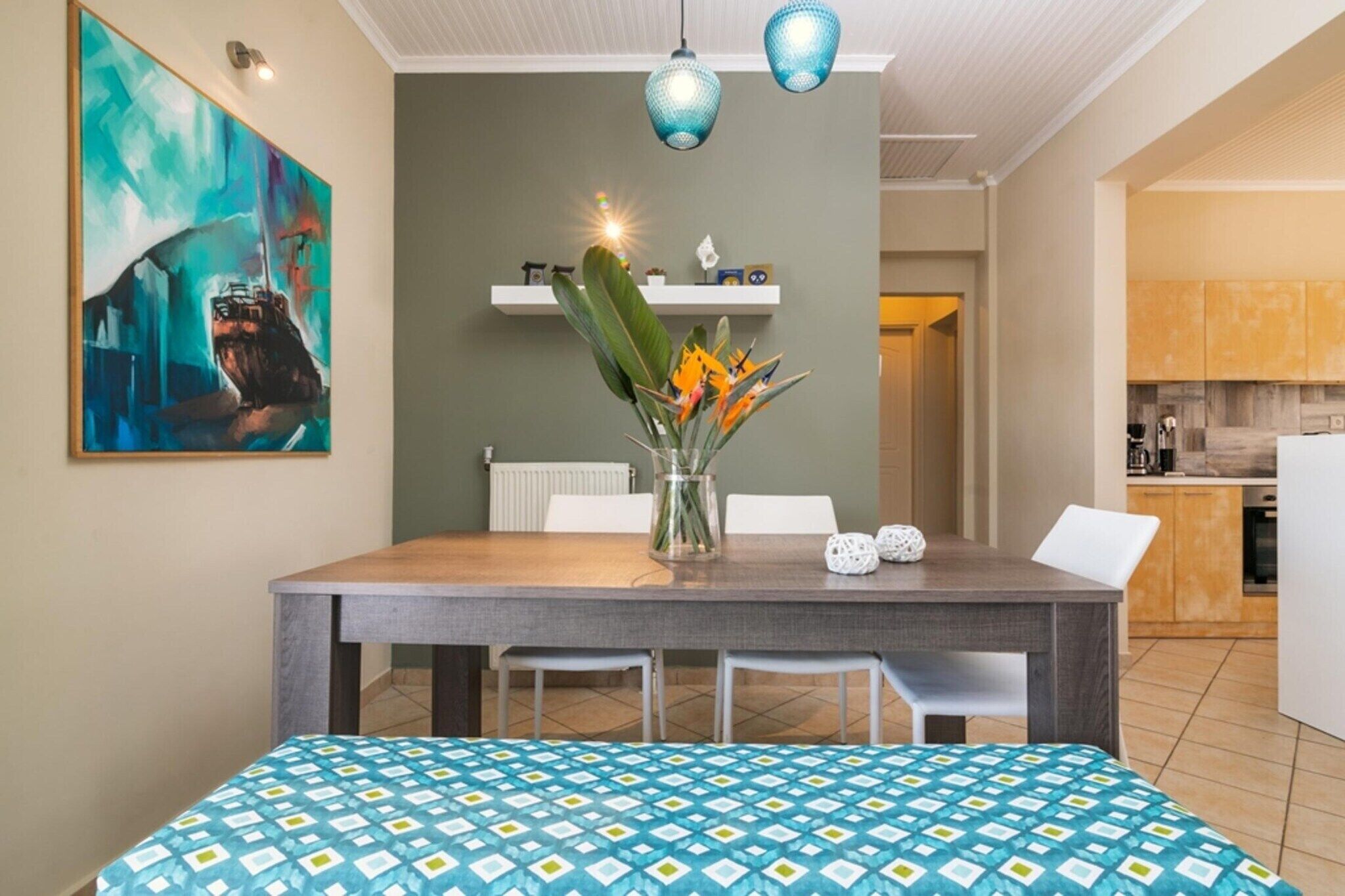 Un comedor con una mesa, sillas, un florero con flores y un cuadro en la pared.