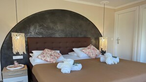 Una cama bien hecha con almohadas y toallas estampadas con motivos florales, una mesita de noche de madera con cajones y un amplio cabecero arqueado.
