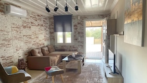 Una sala de estar con pared de ladrillo, un sofá, una mesa de centro, un televisor y un ventanal grande.