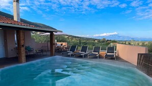 Una piscina infinita en la azotea con sillones, una pérgola y vistas a la montaña.