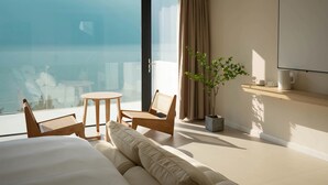 Ein Hotelzimmer mit Balkon, einem Bett, einer Couch, einem kleinen Tisch, zwei Stühlen, einer Zimmerpflanze und einem wandmontierten Fernseher.