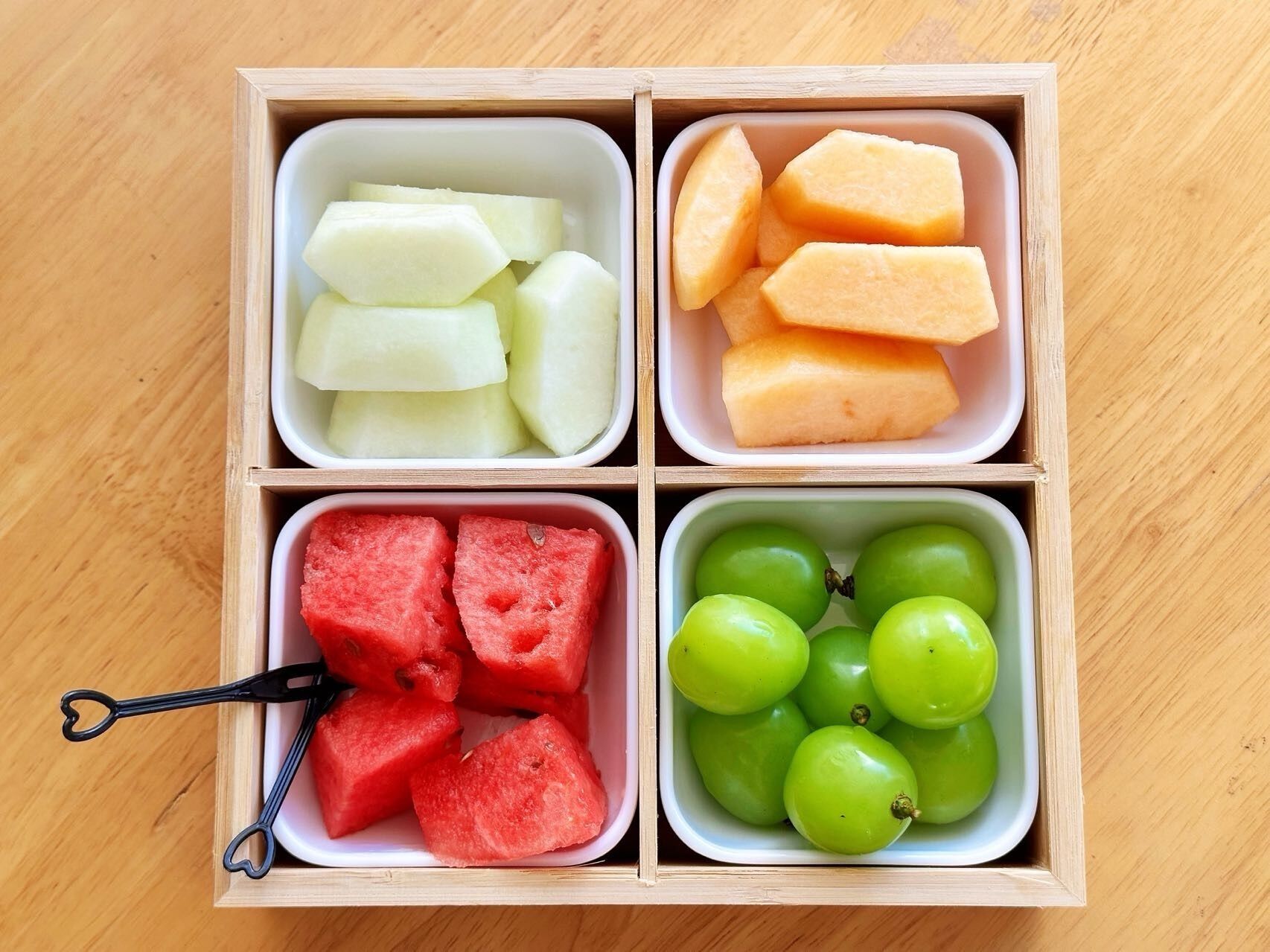 A wooden box divided into four compartments containing different fruits.