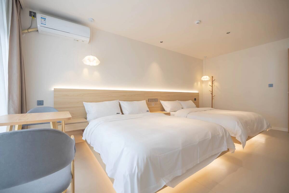 A modern hotel room with two beds, a desk, and a chair.