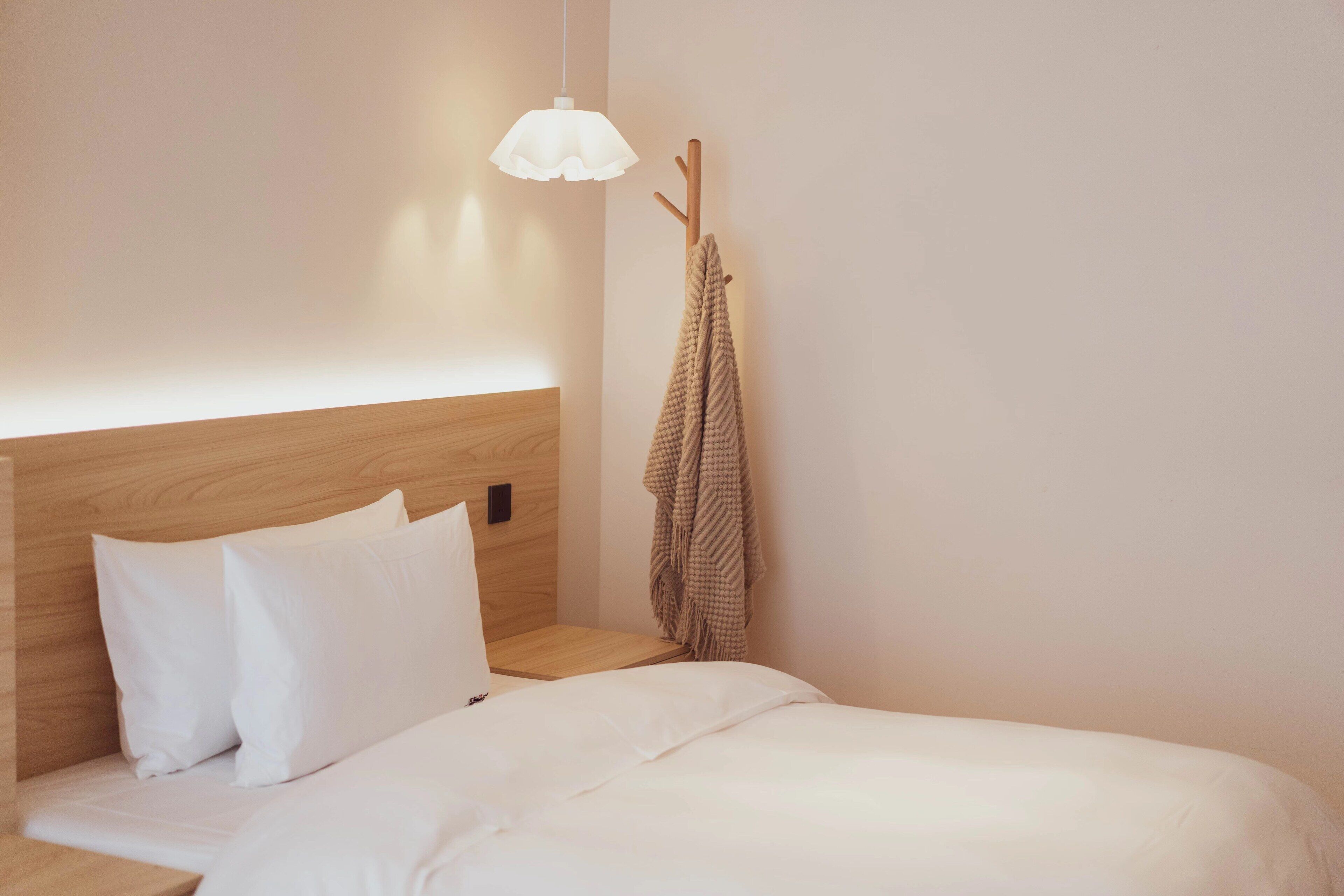 Uma cama bem arrumada com roupa de cama branca, uma cabeceira de madeira e um candeeiro suspenso.