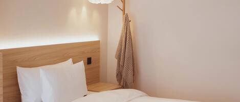 Uma cama bem arrumada com roupa de cama branca, uma cabeceira de madeira e um candeeiro suspenso.