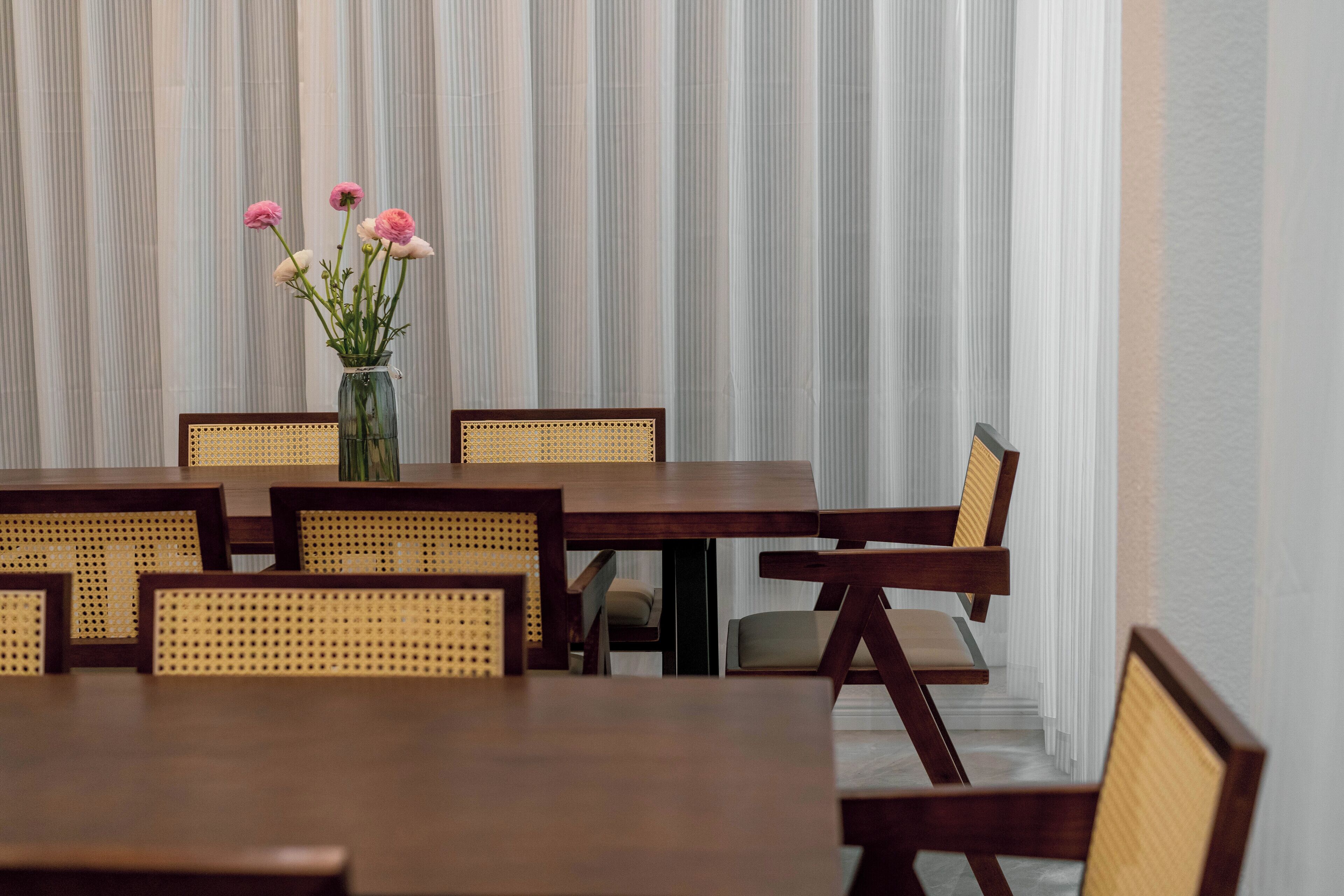 A dining area with a wooden table and chairs, a vase with flowers, and a striped curtain in the background.