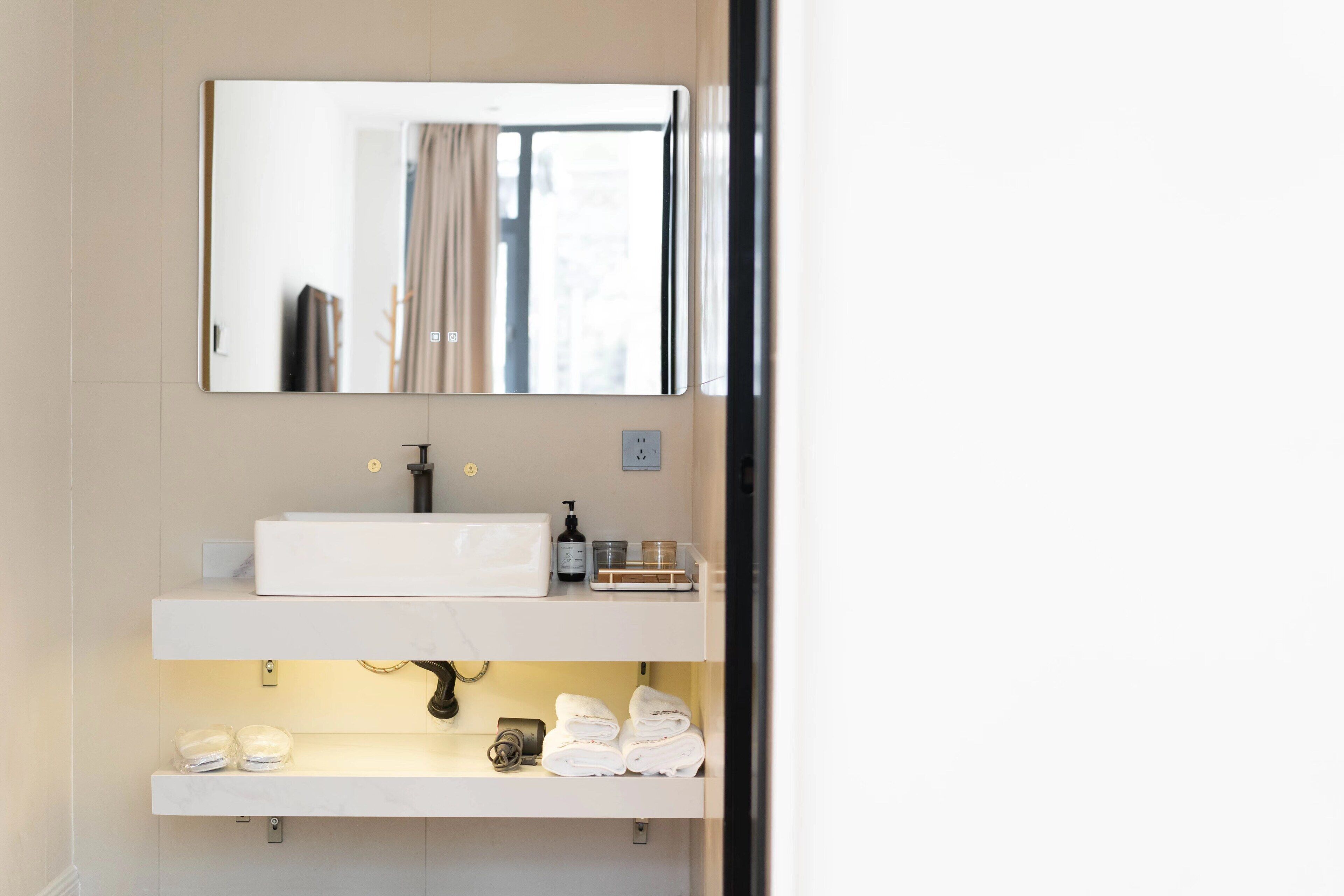 Un baño con un lavamanos blanco, un espejo y un estante con toallas y artículos de aseo.