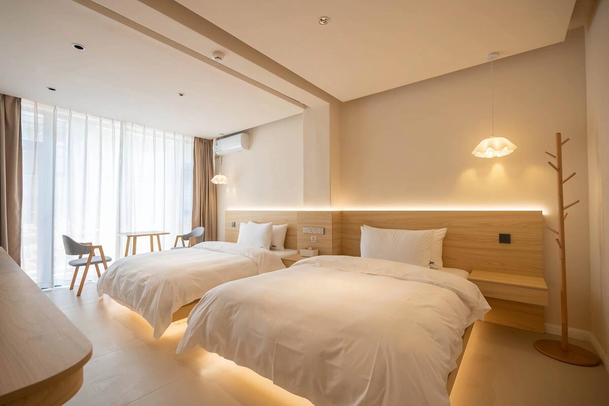 A modern hotel room with two beds, a desk, and a chair.