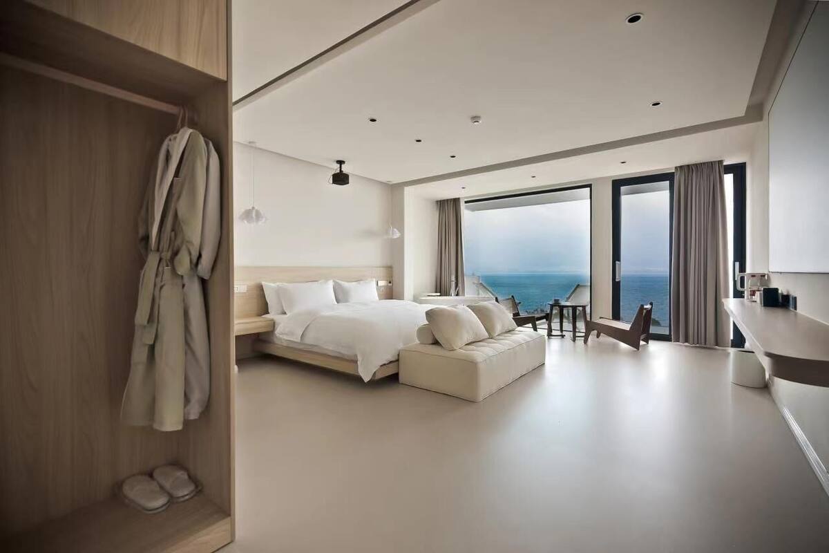 A modern hotel room with a large bed, a seating area, and a view of the ocean.