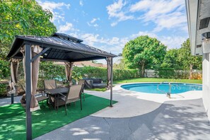 A covered patio area with outdoor furniture, a pool, and a view of a natural landscape.