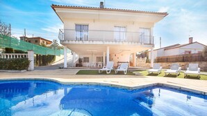 Una casa de dos plantas con piscina, mobiliario de exterior y un balcón.