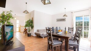 Un comedor con una mesa y sillas de madera, una planta en maceta y un televisor sobre un soporte.