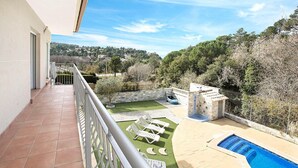Un balcón con piscina, sillas de descanso y vistas a un césped y árboles verdes.
