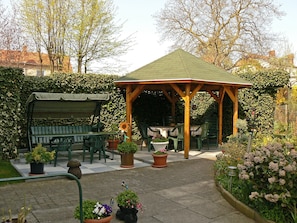 Ein Gartenpavillon mit einem gefliesten Patio, umgeben von Topfpflanzen und einer Bank.