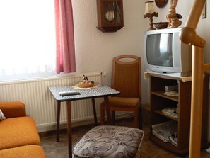 A small living room with a television, a wicker chair, a small table with a basket, and a radiator.