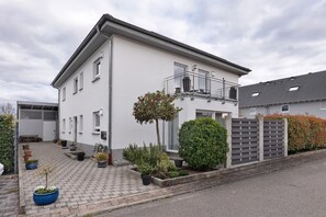 Kaksikerroksinen rakennus, jossa on parveke, ruukkukasveja ja portilla varustettu sisäänkäynti.