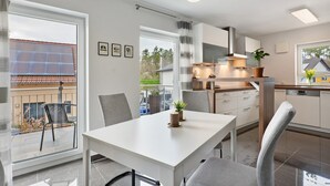 A modern kitchen with white cabinets, a dining table, and chairs. There is a window with a view of the outside. - Apartment 'Am Otterbach' with Balcony and Wi-Fi (Jockgrim)