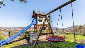 Une structure de jeux en bois, dotée d’un toboggan et de balançoires, installée dans un cadre rural.
