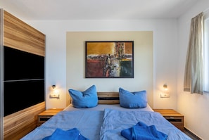 A bedroom with a bed, two nightstands, a wall-mounted TV, and a painting.