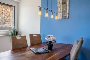 Una mesa de comedor con sillas, un jarrón con flores, un cuadro enmarcado y una lámpara colgante.
