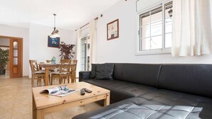 Moderni olohuone, jossa on musta nahkasohva, puinen ruokapöytä ja tuolit. Huoneessa on ikkuna, jossa on valkoiset verhot, ja katosta roikkuu valaisin.