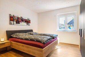 Un dormitorio moderno con una cama de madera, una mesita de noche, una obra de arte en la pared y una ventana con vistas.