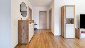 A hallway with wooden flooring, a wooden cabinet with a mirror, a door, and a white cabinet with a television. - Apartment 'Winder 1' with Mountain View and Wi-Fi (Lustenau)