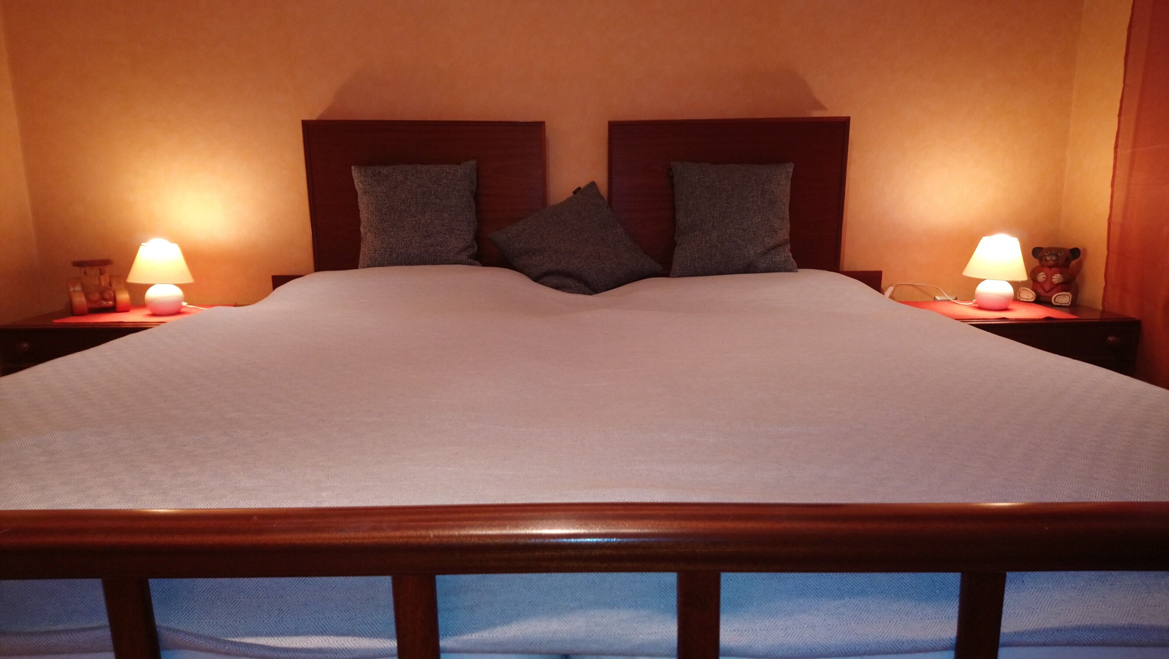 A bed with a wooden headboard, two bedside lamps, and a teddy bear on the nightstand.