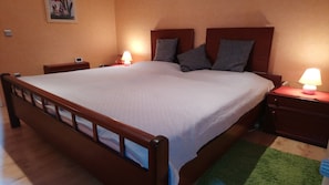 Ett vanligt hotellrum med en säng i trä, två sängbord med lampor, en grön matta och en tavla på väggen.