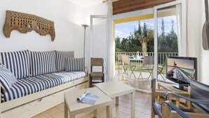 A cozy living area with a striped sofa, a small table, and a TV on a balcony with a view of trees.
