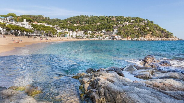 A coastal town with clear waters, rocky shoreline, and buildings on a hillside.