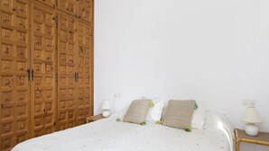 A bedroom with a large wooden wardrobe, a bed with white bedding, two pillows, and two bedside lamps.