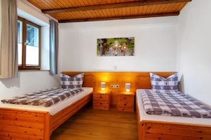 A room with two wooden beds, a window with curtains, a wooden ceiling, and a wall-mounted picture.