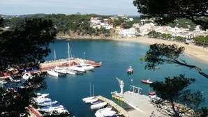 Ein Küstenhafen mit vor Anker liegenden Booten, ein Sandstrand und eine Stadt im Hintergrund.