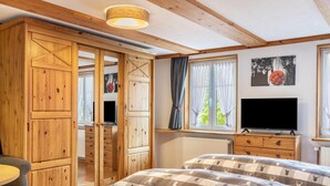 A bedroom with a bed, wooden wardrobe, a television, and a window with curtains.