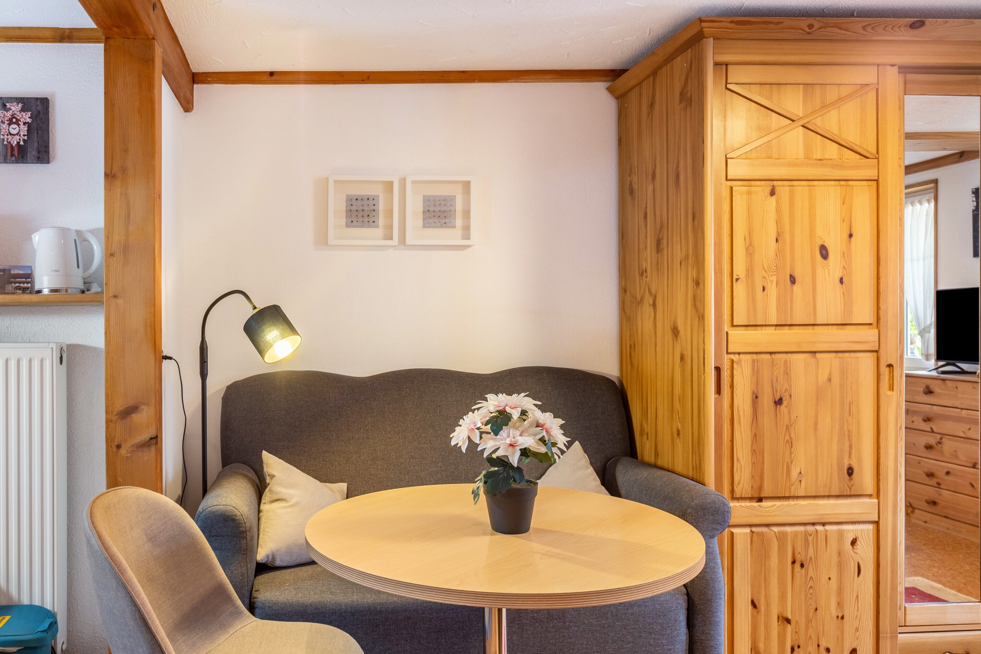 Un salon chaleureux avec un canapé gris, une table ronde en bois, une plante en pot et un meuble en bois.