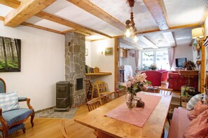 Un interior rústico con vigas de madera a la vista, una chimenea de piedra, una mesa de comedor con sillas y una zona de estar acogedora con un sofá rojo.
