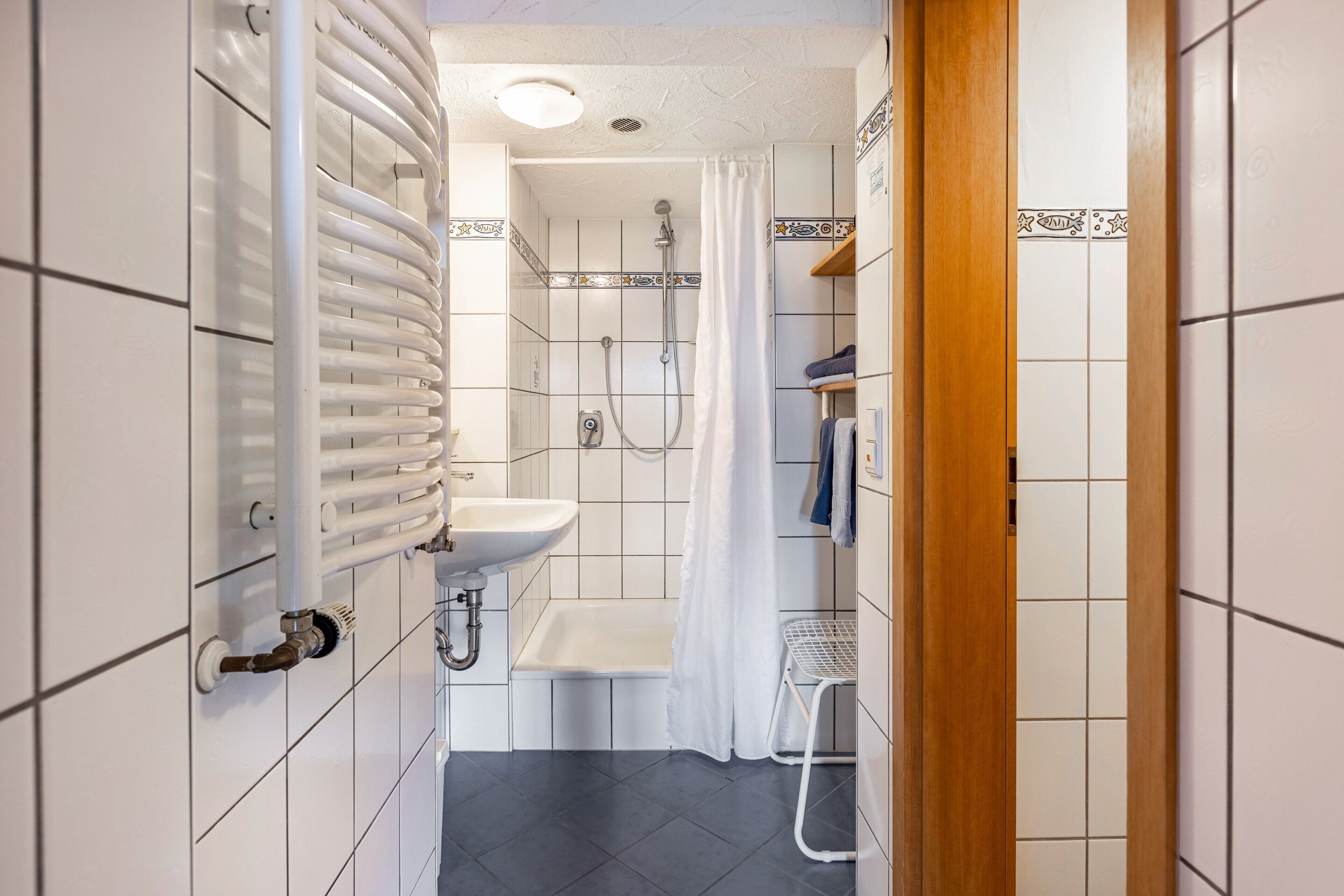 A bathroom with a white sink, shower, and a radiator.