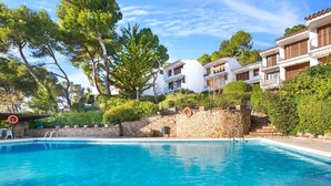 A swimming pool surrounded by stone walls and lush greenery, with multi-story buildings in the background. - Apartment in Spain near Sandy Beach (Llafranc)