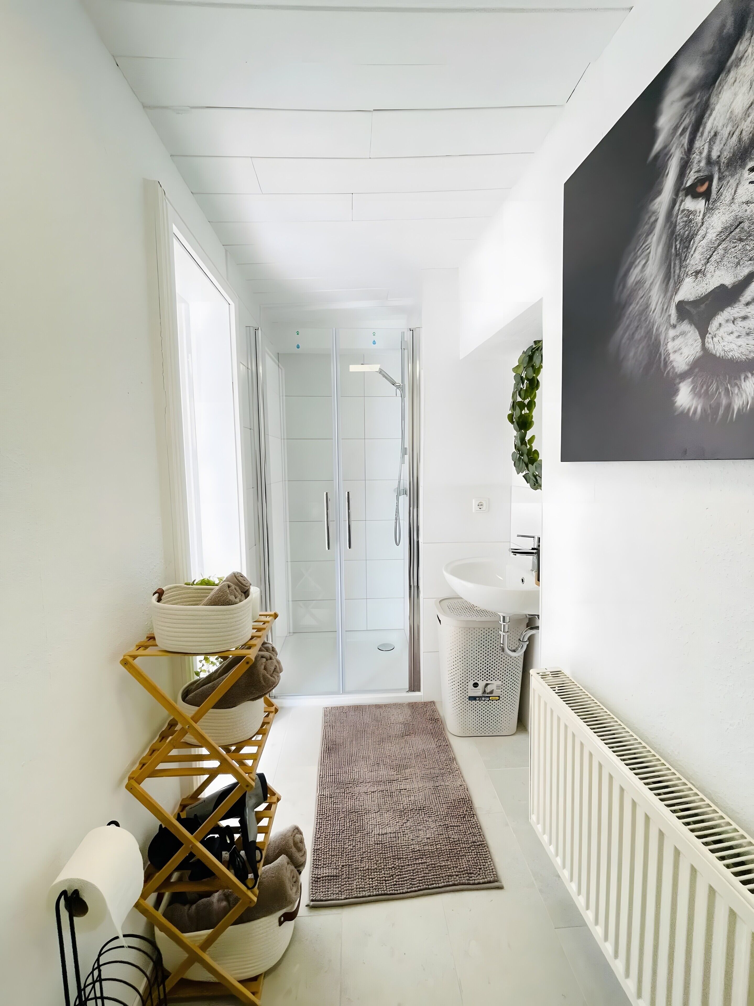 A narrow hallway with a glass shower door, a white radiator, a sink, and a towel rack with folded towels.
