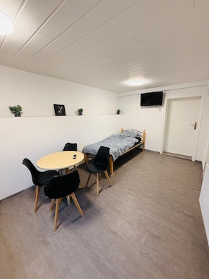 A room with a bed, a table with chairs, a TV on the wall, and small plants on shelves. - Apartment 'D Haus' with Wi-Fi (Arnstein)