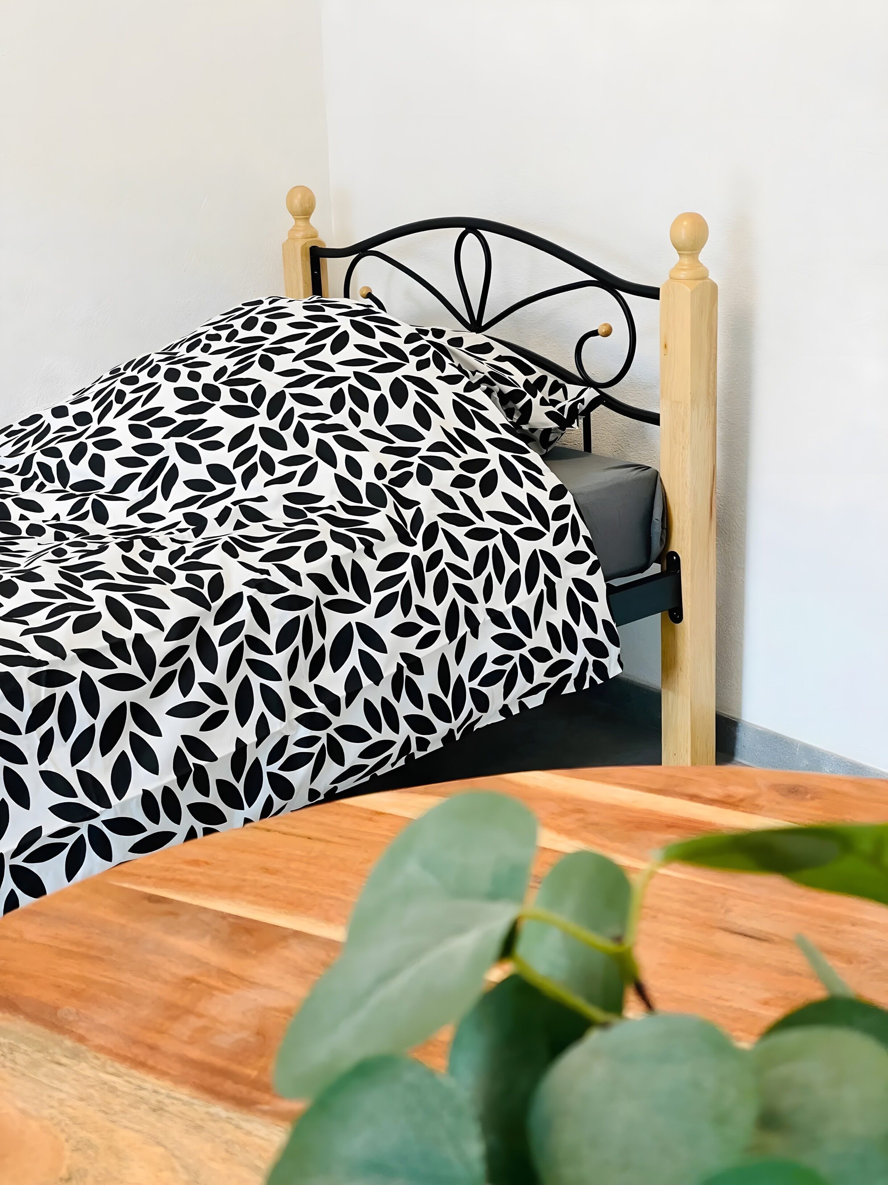 A bed with a black and white leaf pattern bedspread, a wooden headboard, and a grey pillow.