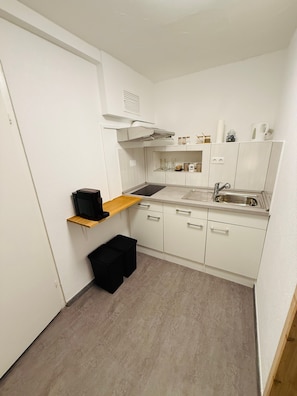 A compact kitchen with white cabinets, a sink, a stove, and a small black trash bin. - Apartment 'D Haus' with Wi-Fi (Arnstein)