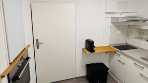 A compact kitchen with white cabinets, a built-in oven, a microwave, a sink, and a small black trash bin. - Apartment 'D Haus' with Wi-Fi (Arnstein)