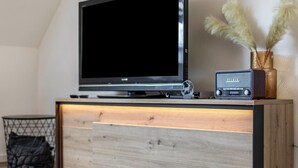 Una sala de estar moderna con un televisor de pantalla plana, una radio antigua y un jarrón decorativo con plumas de pampa.