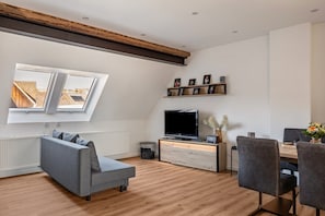 Una sala de estar moderna con sofá, televisor, mesa de comedor, sillas y tragaluz.