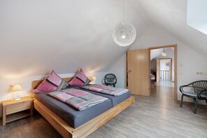 A bedroom with a bed, nightstands, a hanging light fixture, and a view into another room.