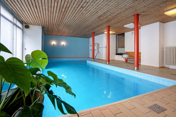 Une piscine intérieure avec un plafond en bois, un sol carrelé et des plantes en pot.